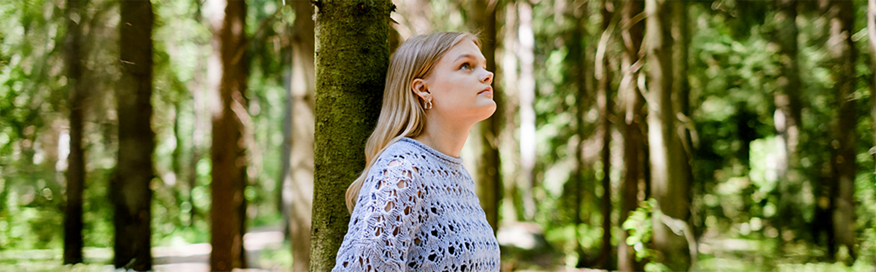 Nuori seisoo metsässä puun vieressä ja katsoo ylöspäin.